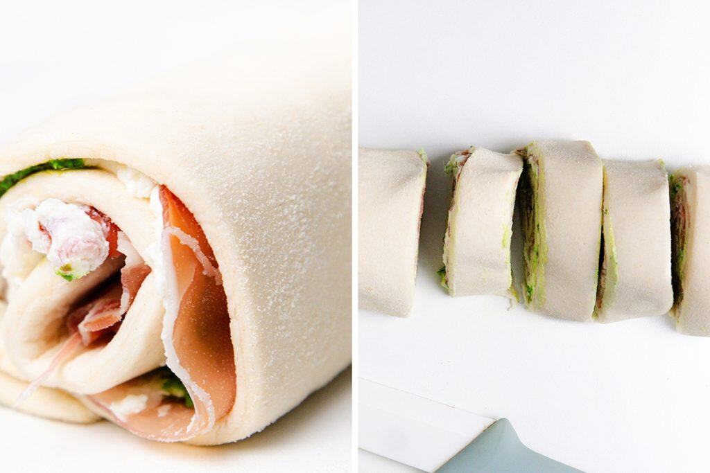 Tampilan jarak dekat dari kincir puff pastry berisi ham dan keju di sebelah kiri, dan di sebelah kanan, gulungan yang diiris menjadi beberapa bagian di permukaan putih dengan pisau terlihat sebagian.