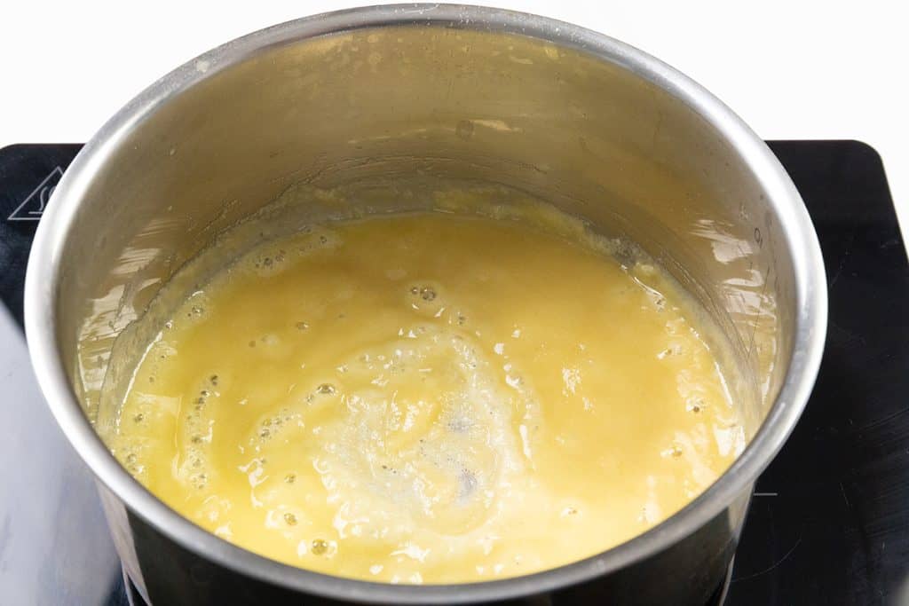A stainless steel pot on a stove contains a bubbling yellow mixture, likely the base for Make-Ahead Gravy or a Pork Gravy Recipe, with melted butter and flour being cooked over heat.