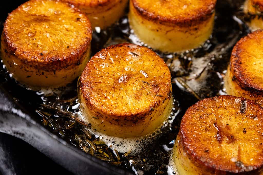 Close-up of crispy potatoes, golden-brown and bubbling in butter with fresh herbs—an irresistible Melting Potatoes recipe in a skillet.
