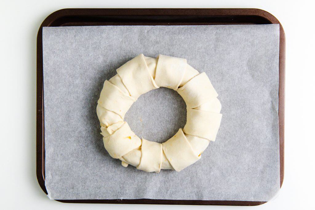 Unbaked puff pastry dough shaped into a festive Christmas wreath with folded segments, ready on a parchment-lined tray—perfect for filling with Brie and fig jam.