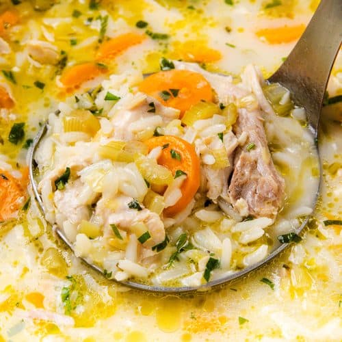 A close-up of a ladle lifting a serving of Chicken and Rice Soup, filled with carrot slices, celery, herbs, and tender chicken pieces in a light broth.