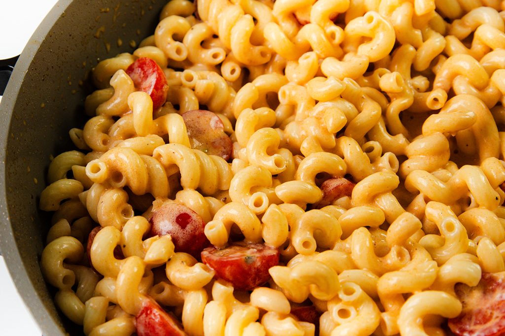 Close-up of creamy steak pasta mixed with melted cheese, macaroni, and pieces of tomatoes in a pan.