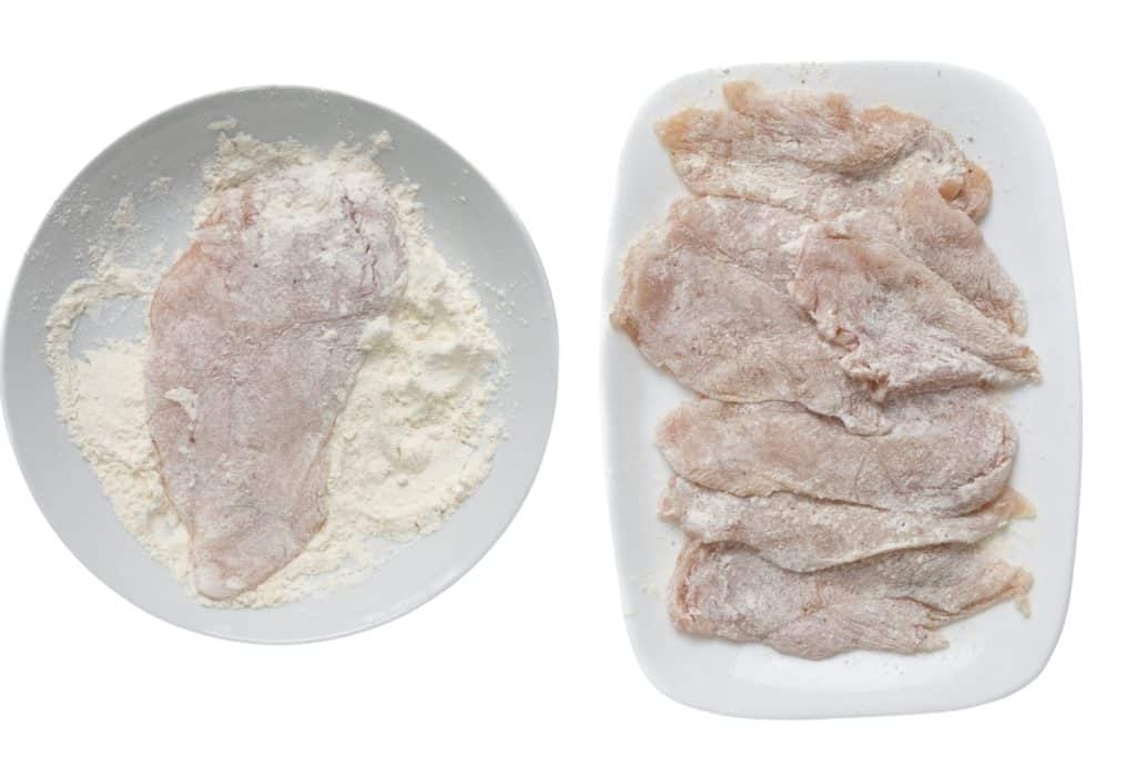 Raw chicken cutlets coated in flour are shown on two white plates, ready to be used in a delicious chicken recipe like Marry Me Chicken. One plate has a single cutlet, while the other displays several floured cutlets side by side.