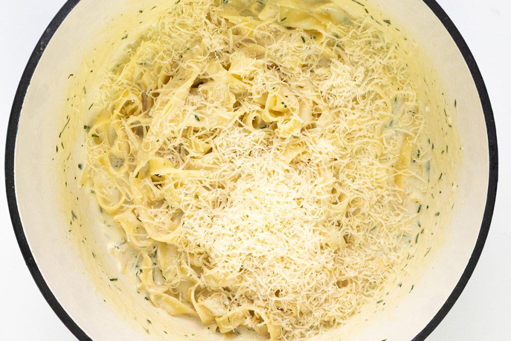 A large white pot filled with One Pot Creamy Garlic Fettuccine Alfredo, topped with a generous layer of grated parmesan cheese.