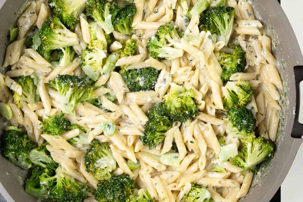 A close-up of penne pasta and broccoli florets in a creamy garlic pasta sauce, all served together in a large pan for an easy one-pot pasta meal.