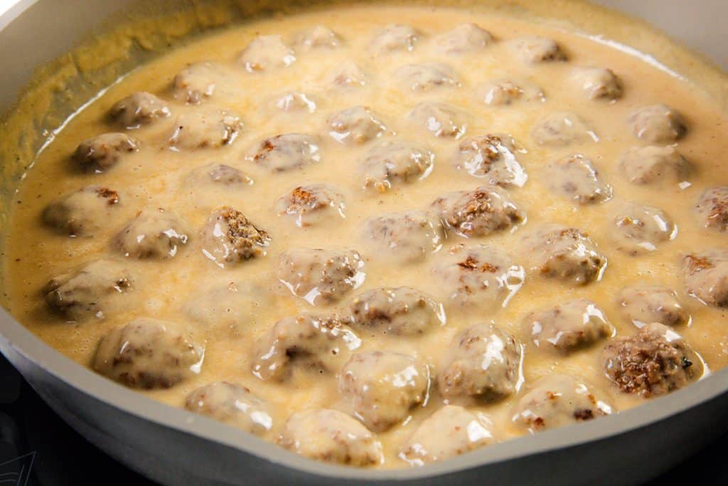 A pan filled with Swedish Meatballs simmering in a creamy gravy, the light brown sauce evenly coating each meatball. This classic Swedish Meatballs Recipe showcases tender meat in a rich, flavorful sauce.