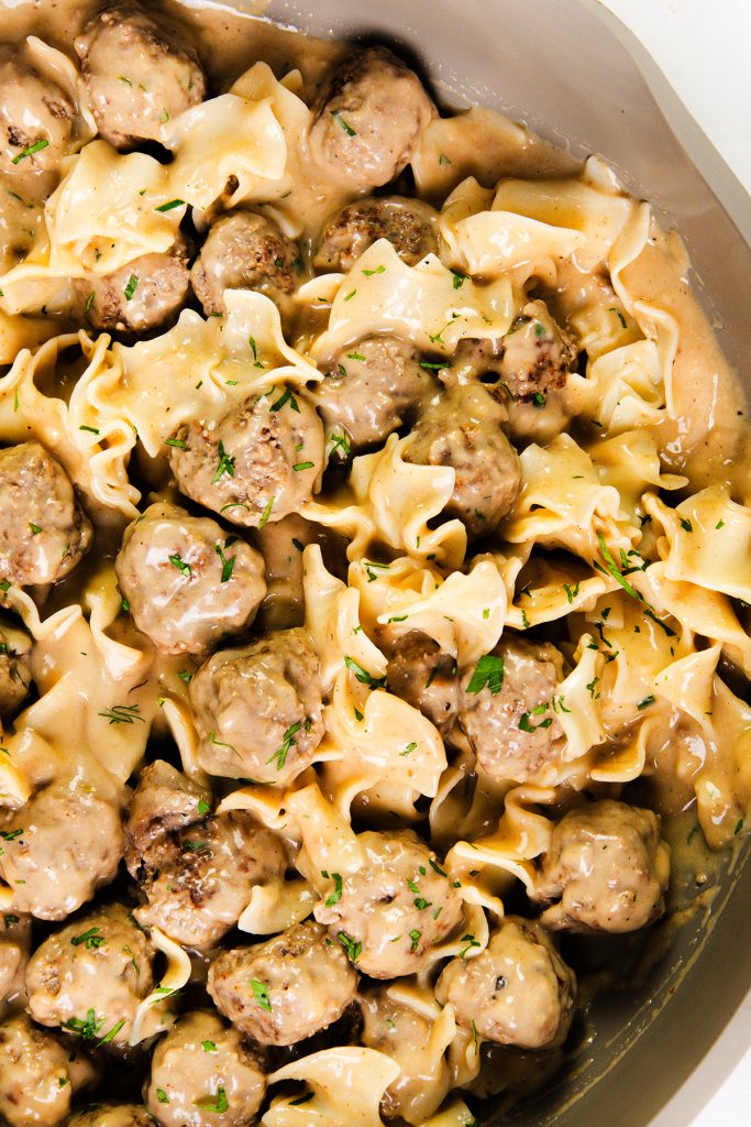Swedish meatballs and egg noodles covered in creamy gravy, garnished with chopped herbs, served in a shallow pan.