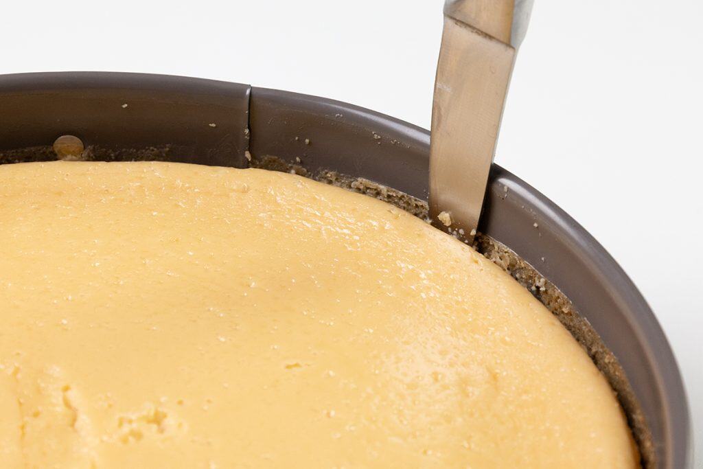 A knife is being used to loosen the edge of a rich Irish cream cheesecake from the sides of a springform pan.