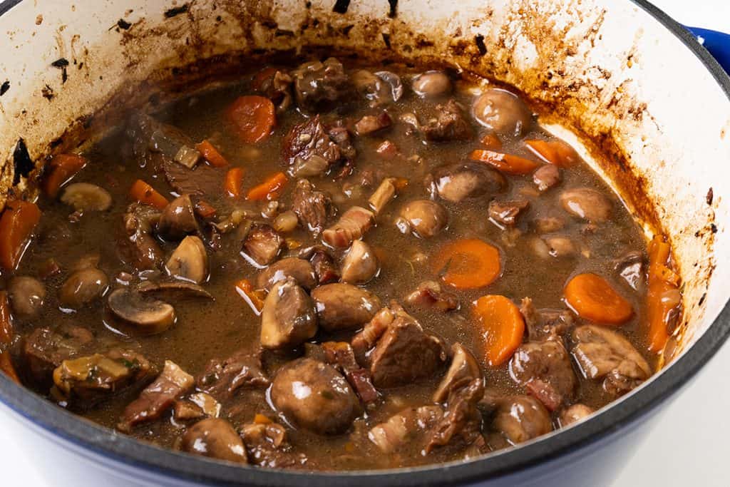 A pot of hearty beef stew with chunks of beef, sliced carrots, mushrooms, and a rich brown Guinness broth simmers in a large enamel Dutch oven.