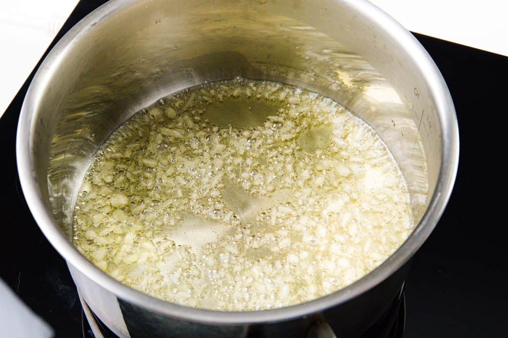 A stainless steel pot on a stovetop with finely chopped garlic sizzling and browning in hot oil, the first step in preparing flavorful cilantro lime rice.