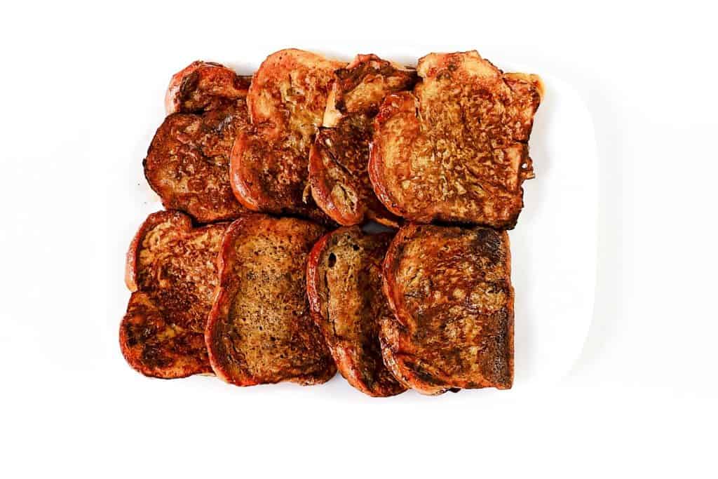 Eight slices of golden-brown French Toast are arranged side by side on a white plate against a crisp white background.