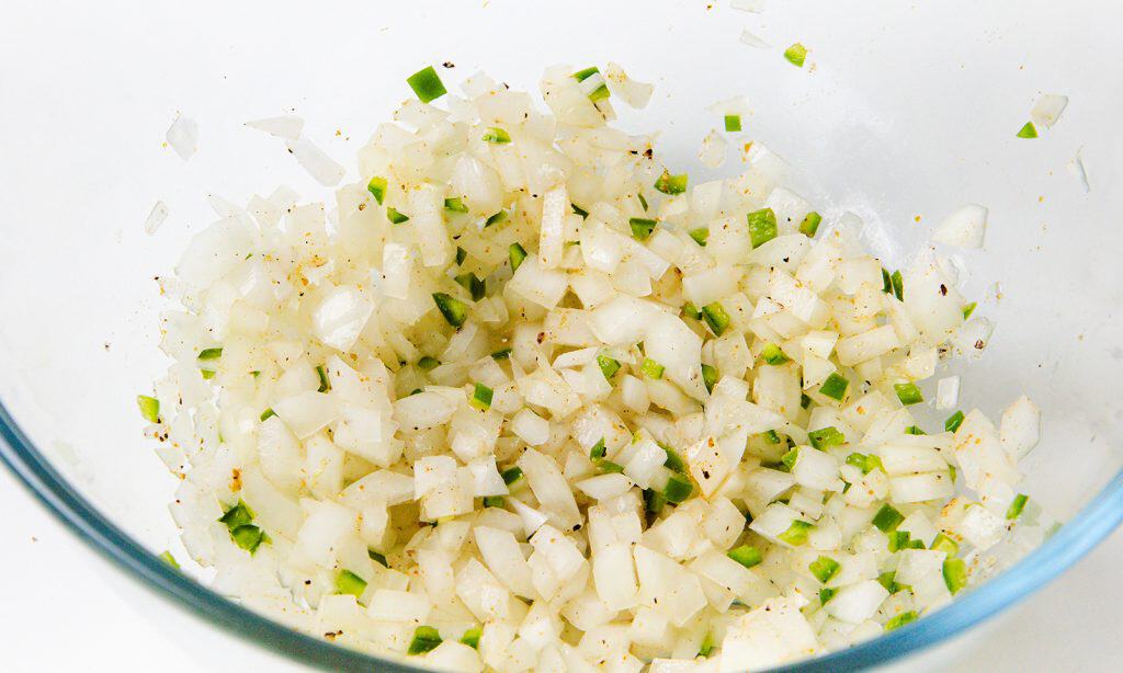 A glass bowl filled with finely chopped white onions and small pieces of green peppers, lightly seasoned with black pepper, creates a classic Pico de Gallo—a fresh salsa often enjoyed as a Mexican condiment.