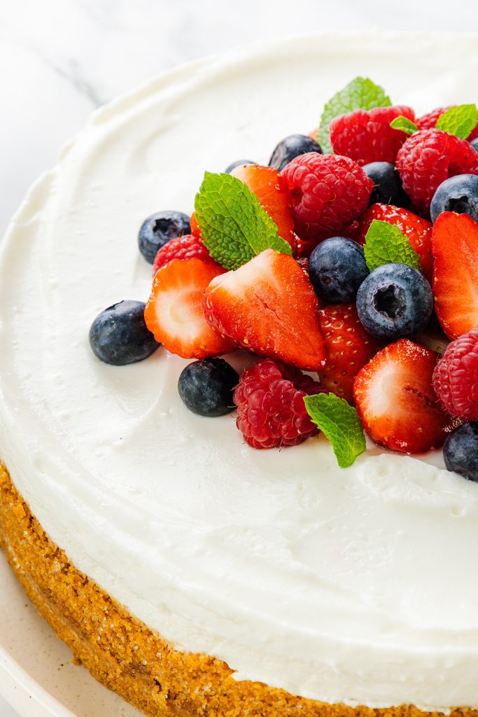 A creamy no-bake cheesecake topped with fresh strawberries, raspberries, blueberries, and mint leaves, set on a golden graham crust—an easy dessert perfect for any occasion.