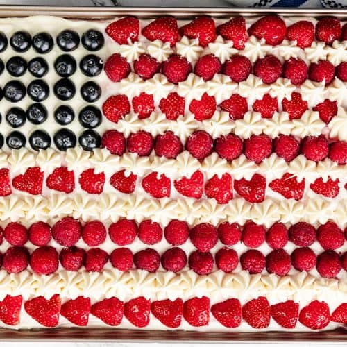 A Patriotic Dessert, this American Flag Cake is a rectangular Red Velvet Sheet Cake topped with blueberries, rows of strawberries and raspberries as red stripes, and white frosting piped as stars and stripes.