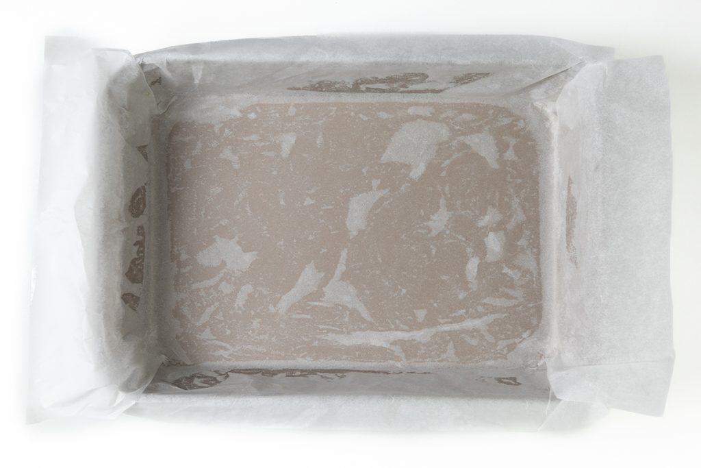 A rectangular baking pan lined with crinkled parchment paper, ready for salted caramel bars, is viewed from above on a white background. The paper neatly overlaps the edges of the pan.