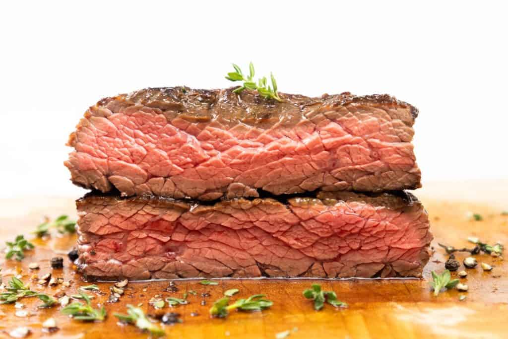 Two thick slices of juicy, medium-rare skillet steak stacked on a wooden cutting board, garnished with fresh herbs and cracked pepper, showcasing their perfectly pink interior.