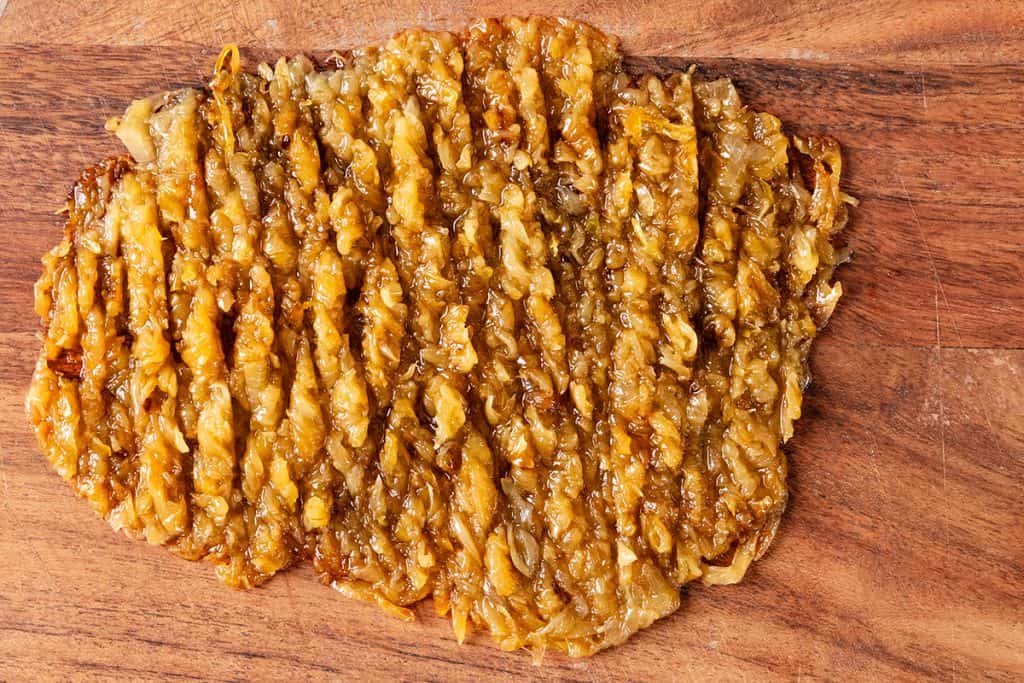 Chopped golden-brown fried onions arranged in an oval shape on a wooden cutting board, perfect for dipping into a rich caramelized onion dip.
