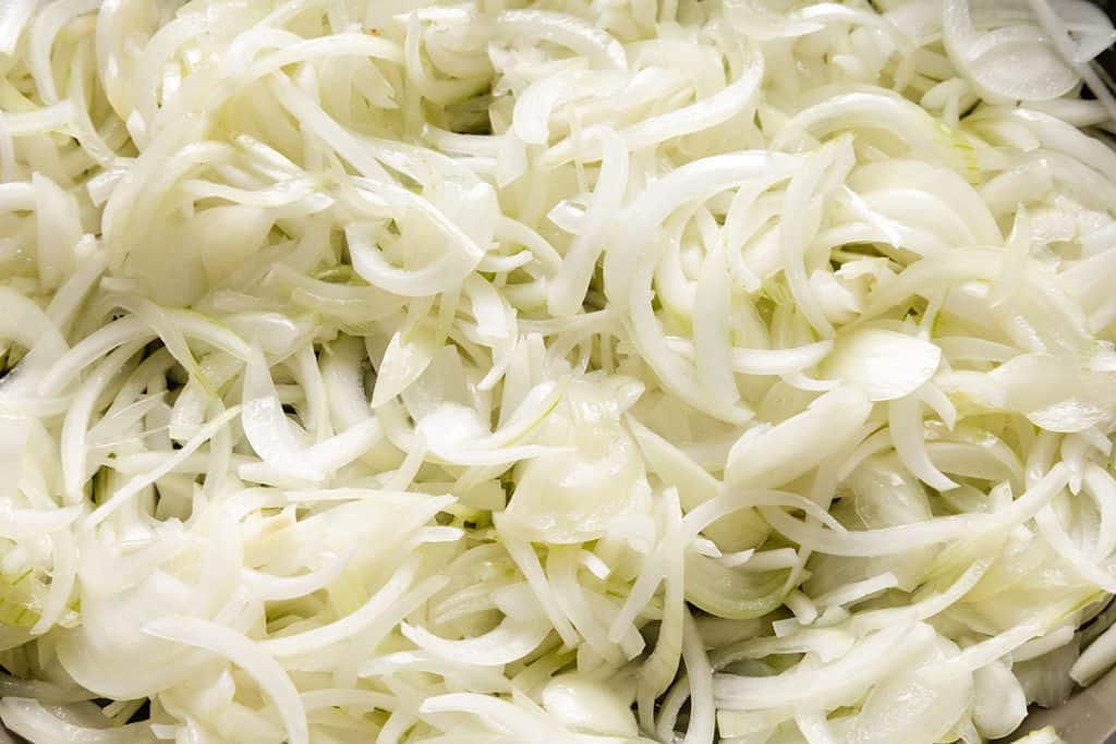 A close-up of a large pile of thinly sliced white onions, showing their translucent layers and curved shapes&mdash;perfect for creating a flavorful Caramelized Onion Dip.