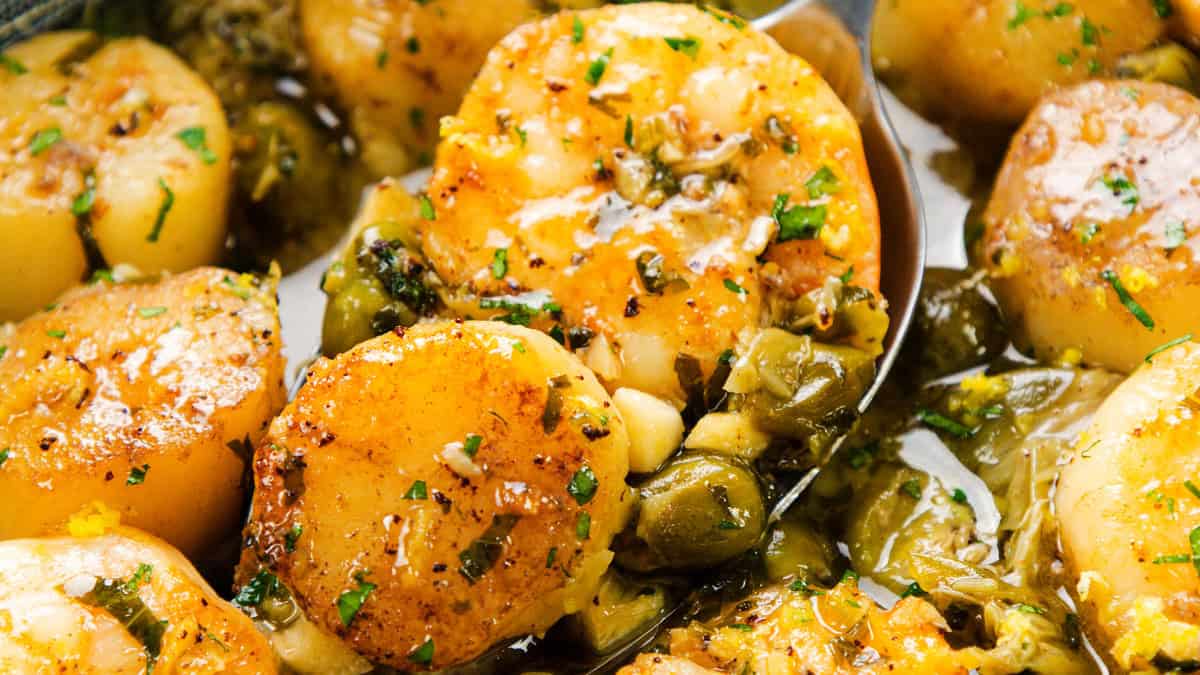 Seared scallops garnished with chopped herbs and surrounded by a savory green sauce with capers. The golden brown scallops are juicy and flavorful, accented by a rich brown butter garlic sauce that enhances every bite.
