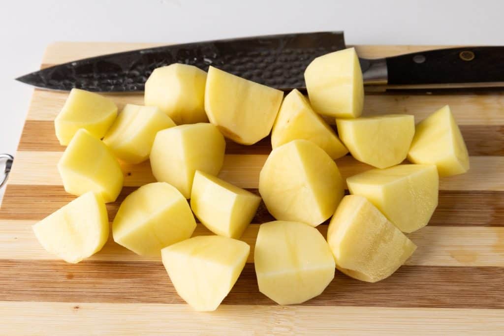 Chopped potatoes on a wooden cutting board, perfect for making Greek Lemon Potatoes, with a large kitchen knife placed behind them.