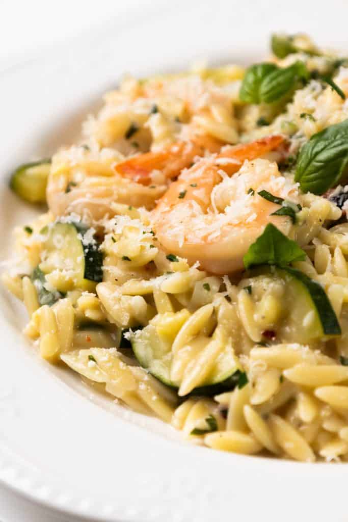 One-Pan Orzo pasta with zucchini, shrimp, fresh basil, and grated parmesan served on a white plate.