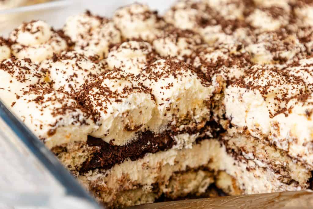 A close-up of a homemade Hot Chocolate Tiramisu dessert, showing creamy layers of mascarpone, soaked sponge, and chocolate shavings in a glass dish.