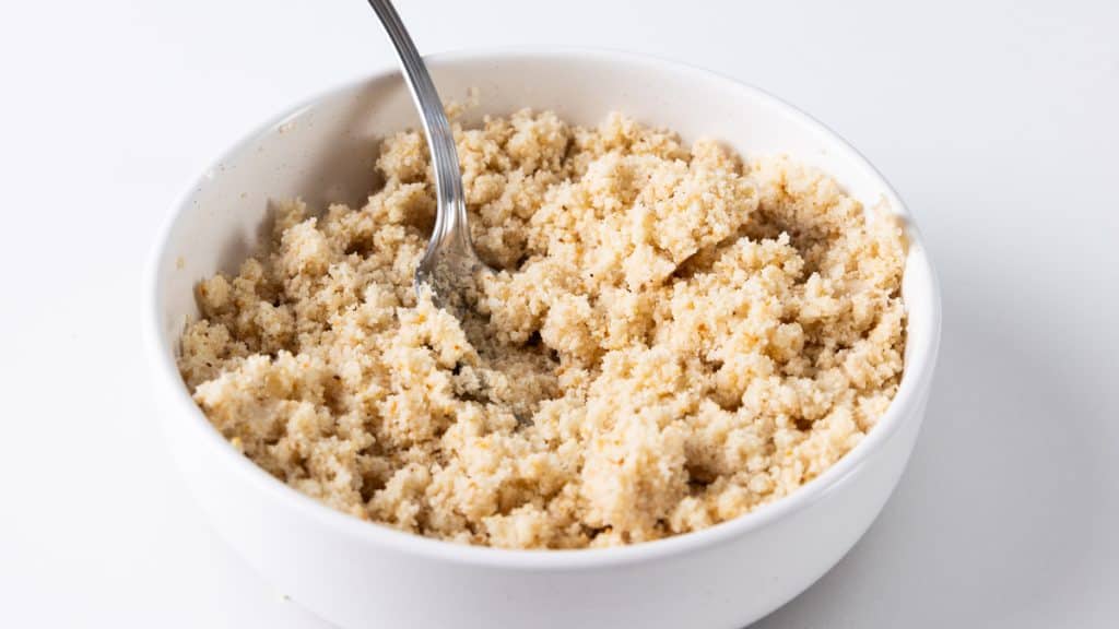 A white bowl filled with a light brown, crumbly meatloaf mixture and a metal spoon, placed on a white surface—perfect for shaping into delicious Meatloaf Burgers.