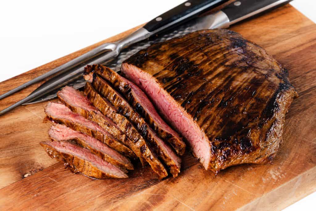 Sliced grilled miso-glazed steak on a wooden cutting board with a carving knife and fork beside it. The steak is cooked medium rare, showing a pink center with hints of savory garlic in every bite.