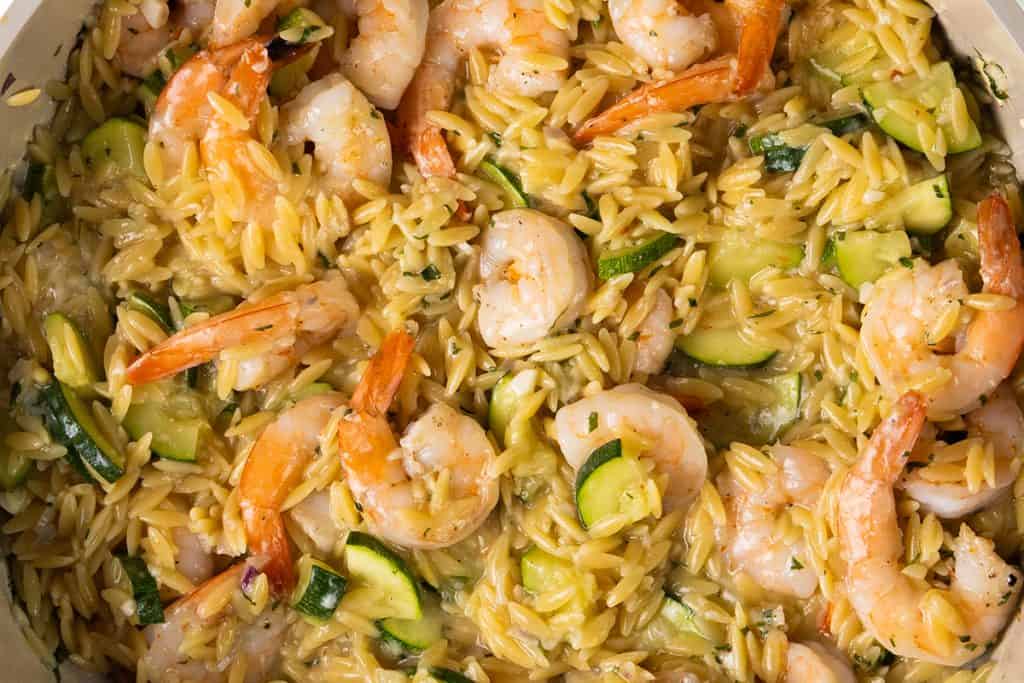 Cooked shrimp, orzo pasta, and zucchini slices are mixed together in a creamy sauce, creating a delicious one-pan orzo dish that fills the pan with flavor.