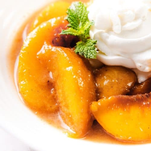 Sliced peaches in syrup, topped with a swirl of whipped cream and a sprig of mint, served in a white bowl—a delightful Peaches and Cream dessert.