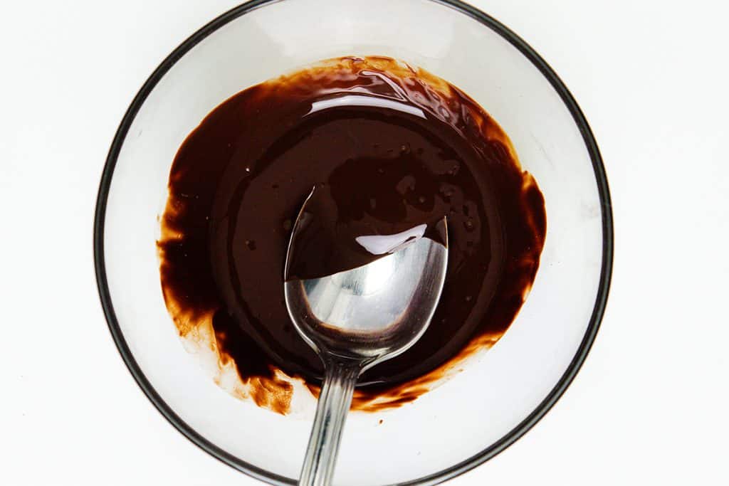 A clear bowl filled with melted chocolate and a metal spoon, shot from above against a white background, evokes the rich indulgence of ice cream desserts—especially when paired with fresh mint or swirled into creamy mint chocolate chip ice cream.