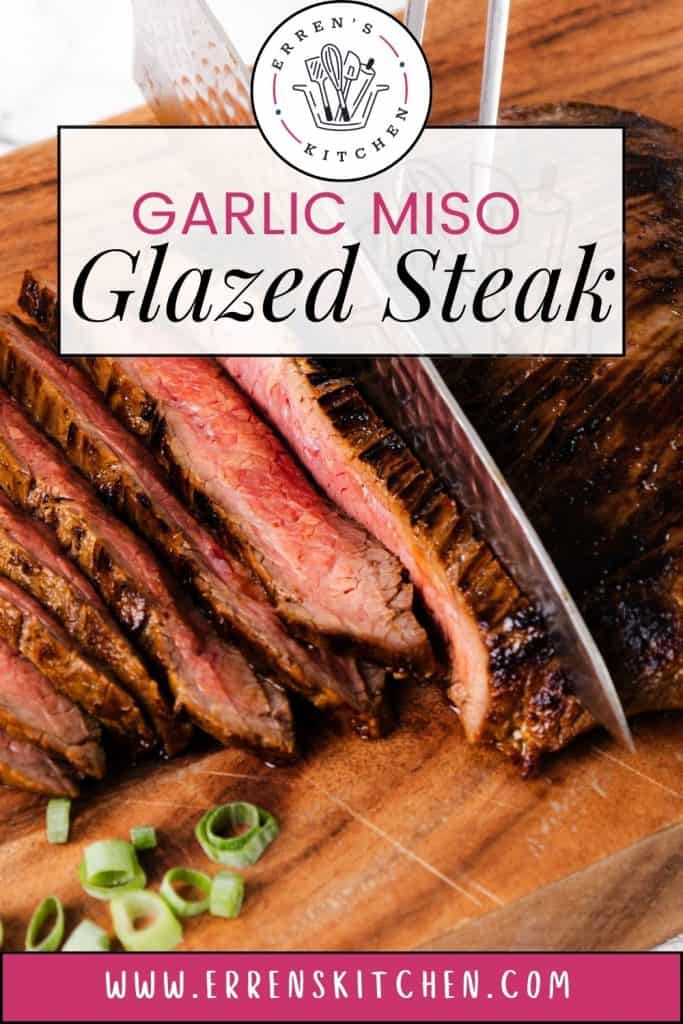 A knife slices a medium-rare steak on a wooden board. The juicy Glazed Steak is labelled “Garlic Miso Glazed Steak,” highlighting its rich flavors. Green onions are scattered nearby, adding freshness to the miso-infused creation. Website: www.errenskitchen.com.
