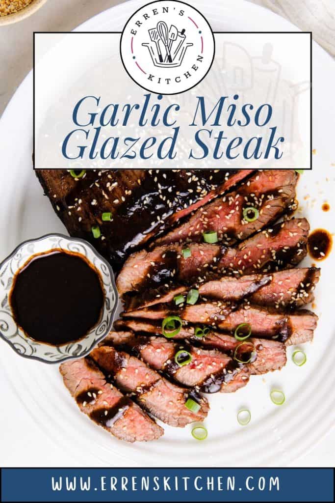Sliced steak topped with green onions and sesame seeds, served with a small bowl of dark sauce on a white plate, featuring the text “Garlic Miso Glazed Steak.” Rich miso and savory garlic combine to create a perfectly glazed steak full of bold flavor.
