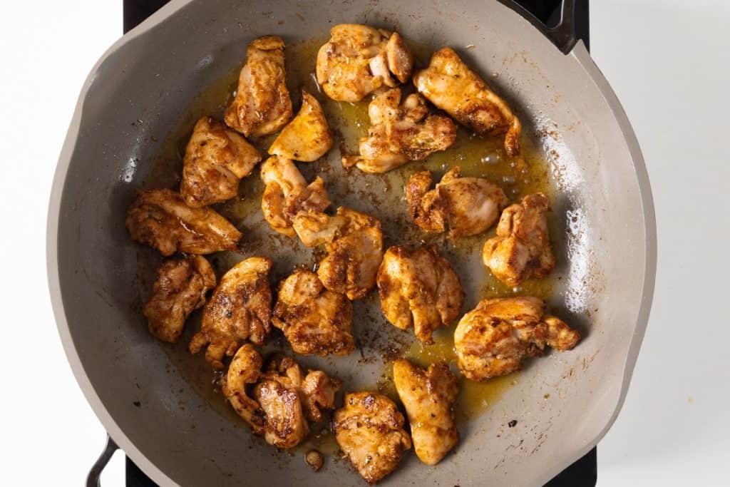 Chunks of seasoned chicken cooking in a gray skillet, sizzling in oil over a stovetop&mdash;the perfect start to a flavorful one-pot chicken and rice dish.