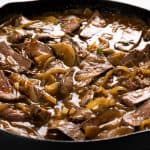 Sliced steak and sautéed onions in a savory brown gravy, served in a black cast iron skillet.