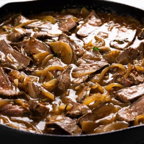Sliced steak and saut&eacute;ed onions in a savory brown gravy, served in a black cast iron skillet.