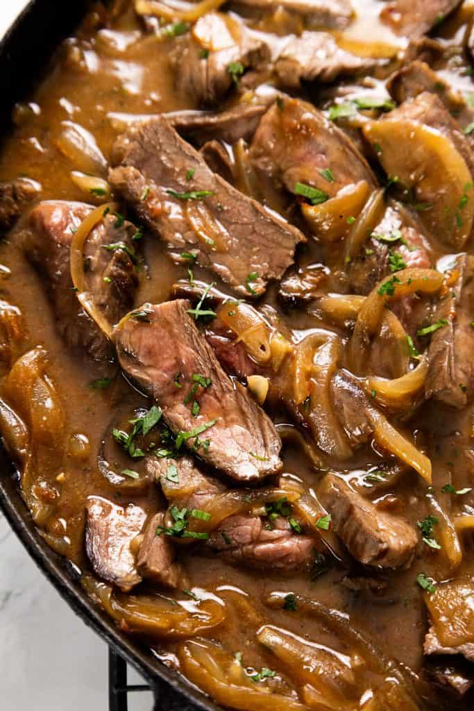 Sliced steak and saut&eacute;ed onions in a brown gravy, garnished with fresh herbs.