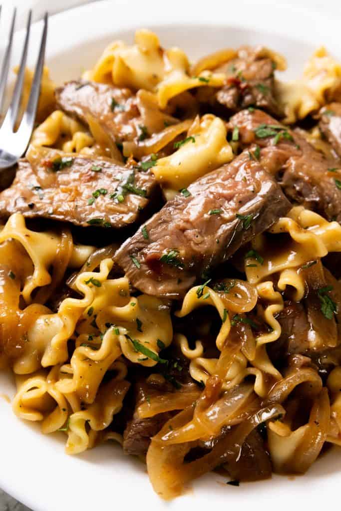 Beef tips with caramelized onions and egg noodles in a savory sauce on a plate.