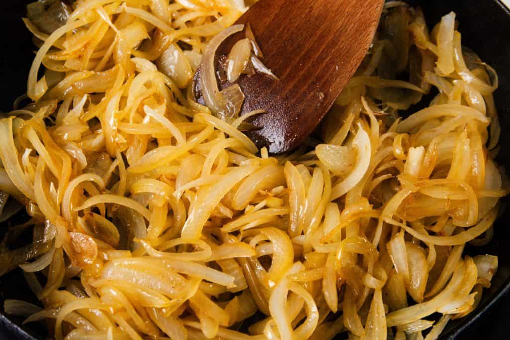Sliced onions saut&eacute;ing in a pan with a wooden spatula.