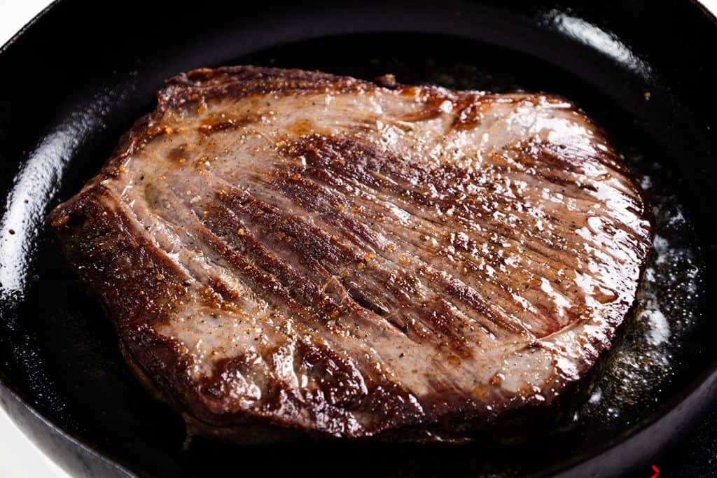 A seasoned beef steak searing in a cast-iron skillet, ready to be served with a sherry onion gravy.