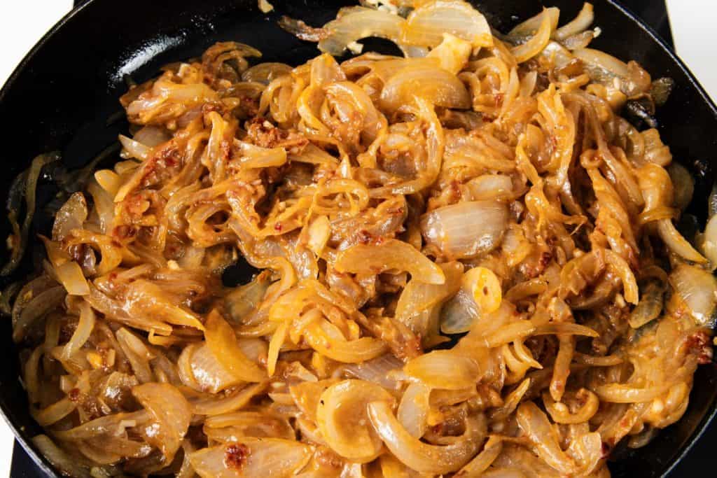 Caramelized onions cooking in a black skillet.