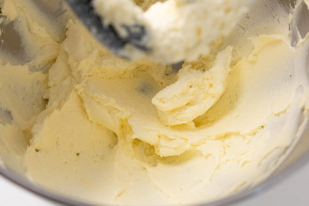 A stand mixer beater mixing pale yellow creamed butter and sugar in a metal mixing bowl for pumpkin spice cookie bars.